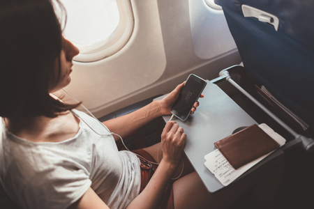 Woman traveling by plane. Girl with a phone in her hands sitting on the airplane.の写真素材