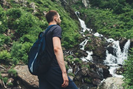 Young man looking at mountain stream in the forest admires nature.の写真素材