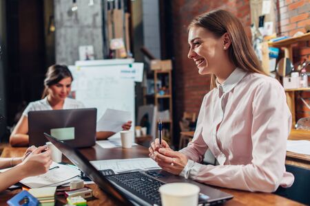 Team of business women working with papers using laptops sitting at desk in officeの写真素材