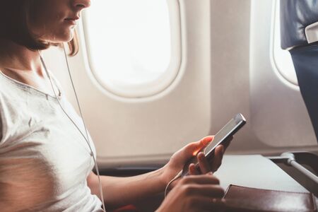 Woman traveling by plane. Girl with a phone in her hands sitting on the airplane.の写真素材