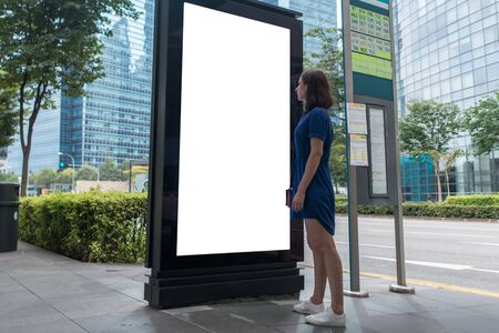 Woman standing near blank advertising lightbox on the bus stop, mock upの写真素材
