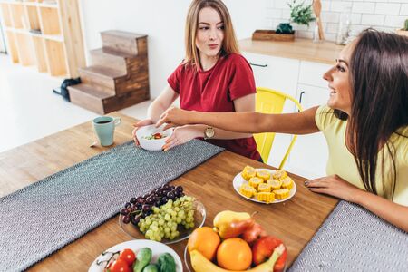 Women friends eating fruits and vegetables in kitchen. Healthy nutrition. Low calorie meal.の写真素材