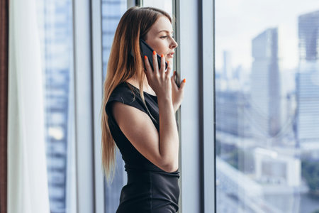 Elegant young female business owner holding documents talking on mobile phone discussing contract...