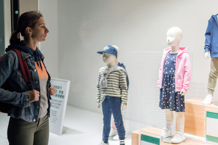Young woman stands near kids wear store window.