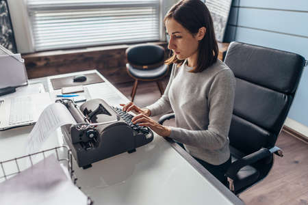 Woman in office at her desk typing on a typewriterの写真素材