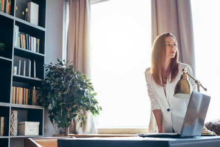 Business woman stands near the workplace leaning on the table.