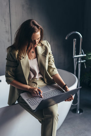 Woman hides at home in the bathroom with her laptop to work.