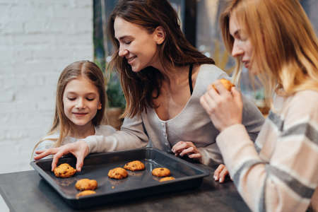 Young woman and her friend are curious about the cookies her daughter madeの写真素材