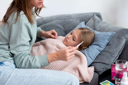 Mom sits next to her daughter and looks at the thermometer after taking her temperatureの写真素材