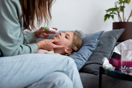 Girl has a runny nose and her mother sprays medicine into her noseの写真素材