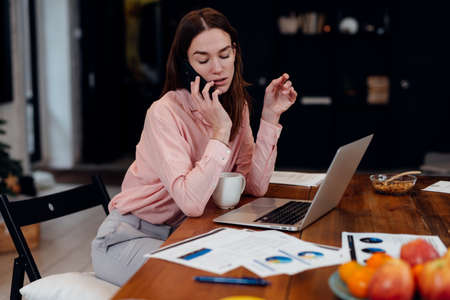 Young woman talking on smartphone while looking at her papers.の写真素材