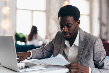 Black man sits at table and works holding document in his hand.の写真素材