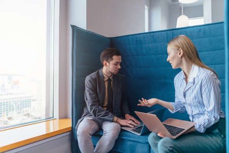 Woman and man sit with their laptops and have informal business conversationの写真素材