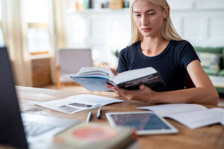 Woman student sitting at table reading book.の写真素材
