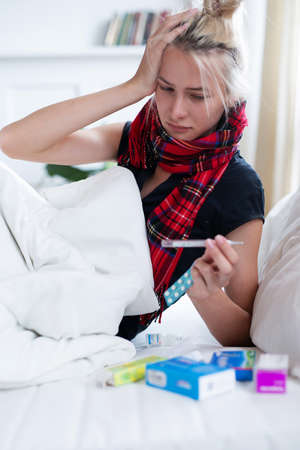 Woman saddened by looking at thermometer because of elevated body temperatureの写真素材