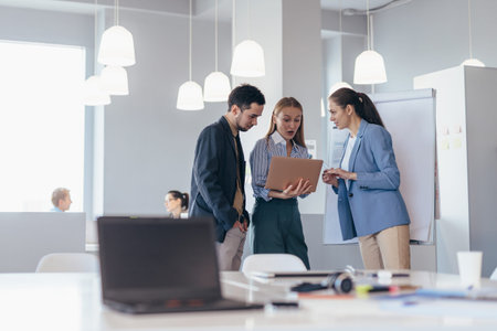 Employees stand in the meeting room with a laptop and discuss business matters