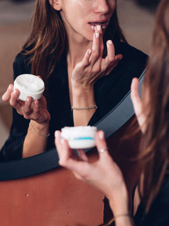 Woman applies a nourishing balm to her lips, moisturizing her skin.の写真素材