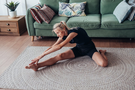 Woman working out at home, doing stretching bends forward while sitting on floorの写真素材