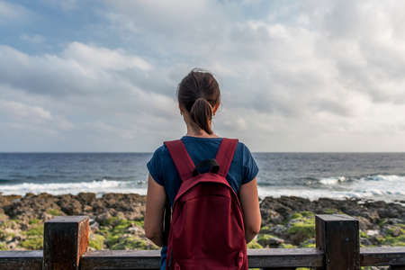 Young woman standing by the shore looking at the sea and the sky.の写真素材