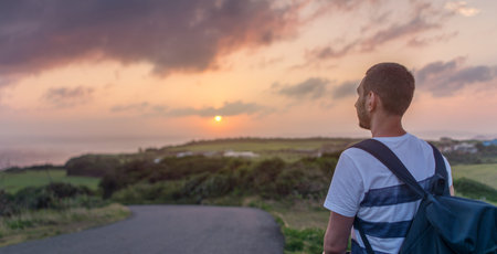 Young man standing on a hill with a bicycle in the evening at sunset