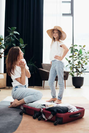 Woman packing suitcase for travel, her daughter dressed up dreaming of tripの写真素材