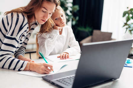 Young woman writes in notebook with girl sitting next to her doing homework.の写真素材