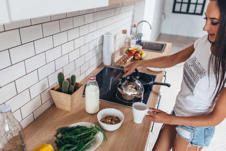 Woman is heating water in a kettle to make coffee.の写真素材