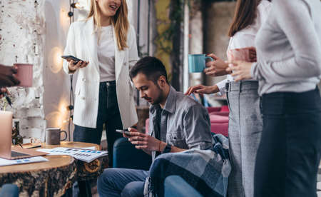 Young man sits with a smartphone while his colleagues talkの写真素材