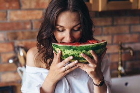 Woman at home eating watermelon in the kitchenの写真素材
