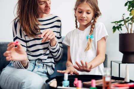 Mother and daughter doing manicure at home, painting nails with nail polishの写真素材