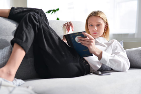 Woman lies on couch and reads book.