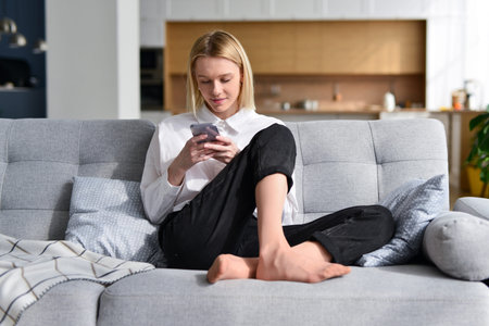 Woman sitting on couch with smartphone at home.