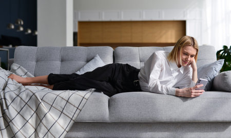 Woman with smartphone at home lying on sofa.