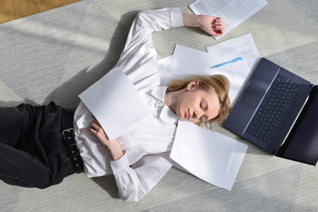 Woman lies on floor among papers tired from her work