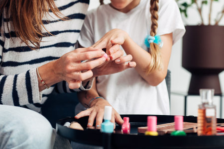 Mother and daughter doing manicure at home, painting nails with nail polish