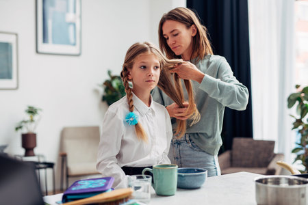 Mother braids her daughters braids before school at breakfast