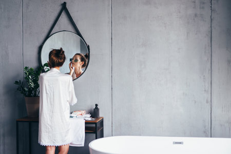 Young woman takes care of her facial skin in bathroomの写真素材