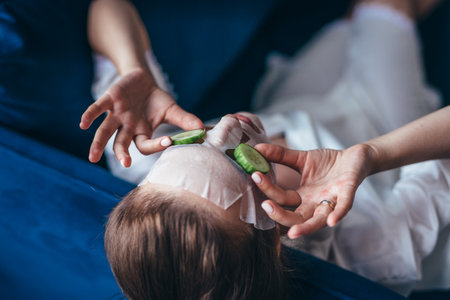 Woman lies on a couch with a sheet mask over her face and cucumber slicesの写真素材