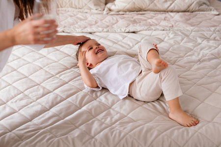 Mother strokes the head of a child lying on the bedの写真素材