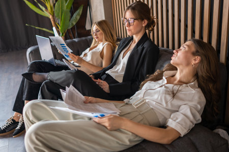 Businesswomen enjoy relaxed conversation in cozy office lounge after team effortの写真素材