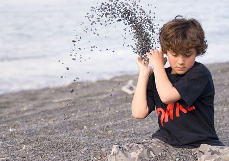 Boy playing with shingle at a beachの写真素材