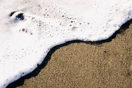 A small wave rolls up the sand like icing spreading on a spongeの写真素材