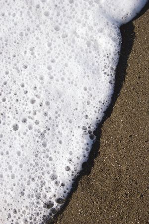 A small wave rolls up the sand like icing spreading on a spongeの写真素材