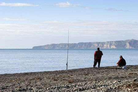 A couple of blokes sitting in the sun on an autumn day pretending to fish. Haumoana Beach, New Zealand. Cape Kidnappers in the backgroundの写真素材