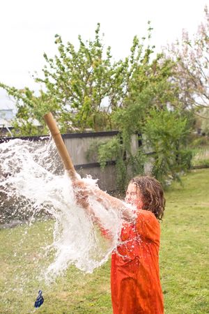 A young male playing with water balloons in the backyard - hitting a balloon with a bamboo stickの写真素材