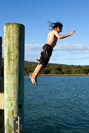 A young caucasian male jumps off the wharf on Rangitoto Islandの写真素材