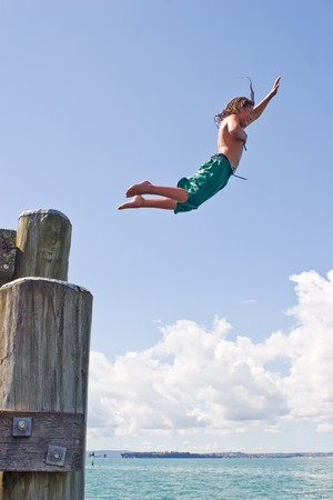 A teenage boy leaps off the wharf at Rangitoto Island in the Hauraki Gulf of New Zealandの写真素材