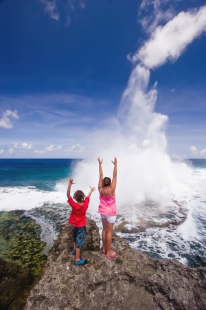 Two youngsters raise their arms as the blowholes put on a spectacular display at Houma on the western side of Tongatapu Island in the Pacific.の写真素材