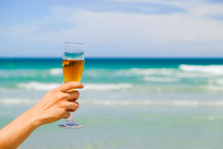 hands of female holding glasses of champagne on tropical sea beachの写真素材