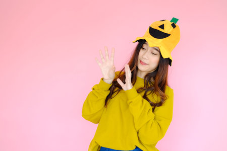portrait asian cute girl wearing casual clothes with halloween hat posing, holiday halloween concept on pink backgroundの写真素材